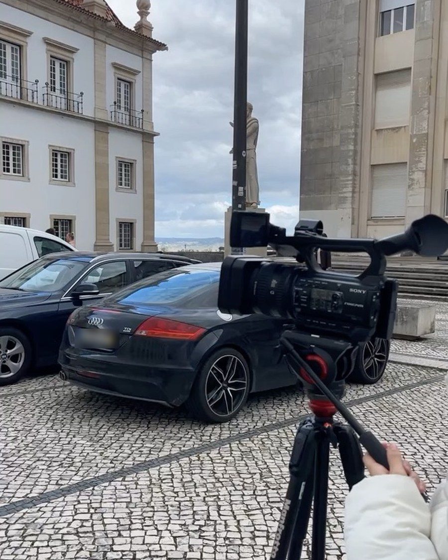 Gravação em campo na Universidade de Coimbra, com câmera de vídeo em tripé e o casario ao fundo