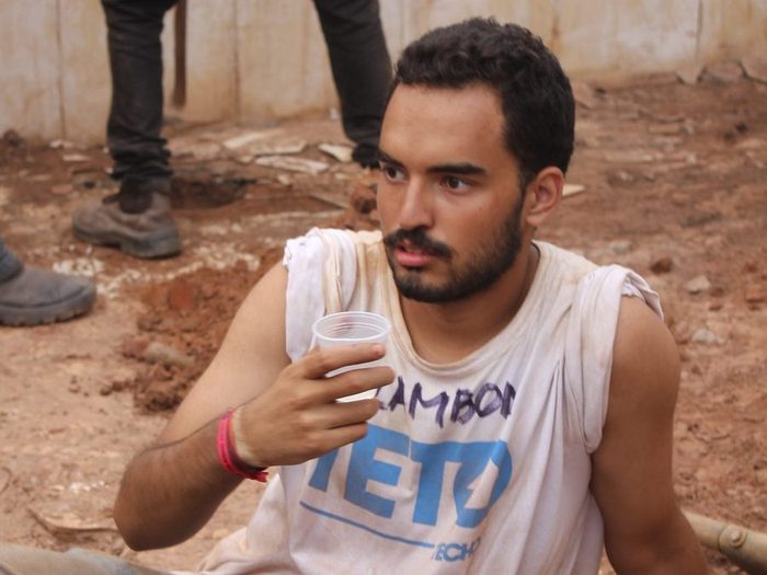 Lucas sentado no chão da obra, camiseta suja de terra, durante uma pausa